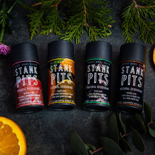 Woodsy photo of Stank Pits natural deodorants in four scents: Blossom, Bright, Fresh, Hombre. The deodorant packaging is compostable with no plastic.