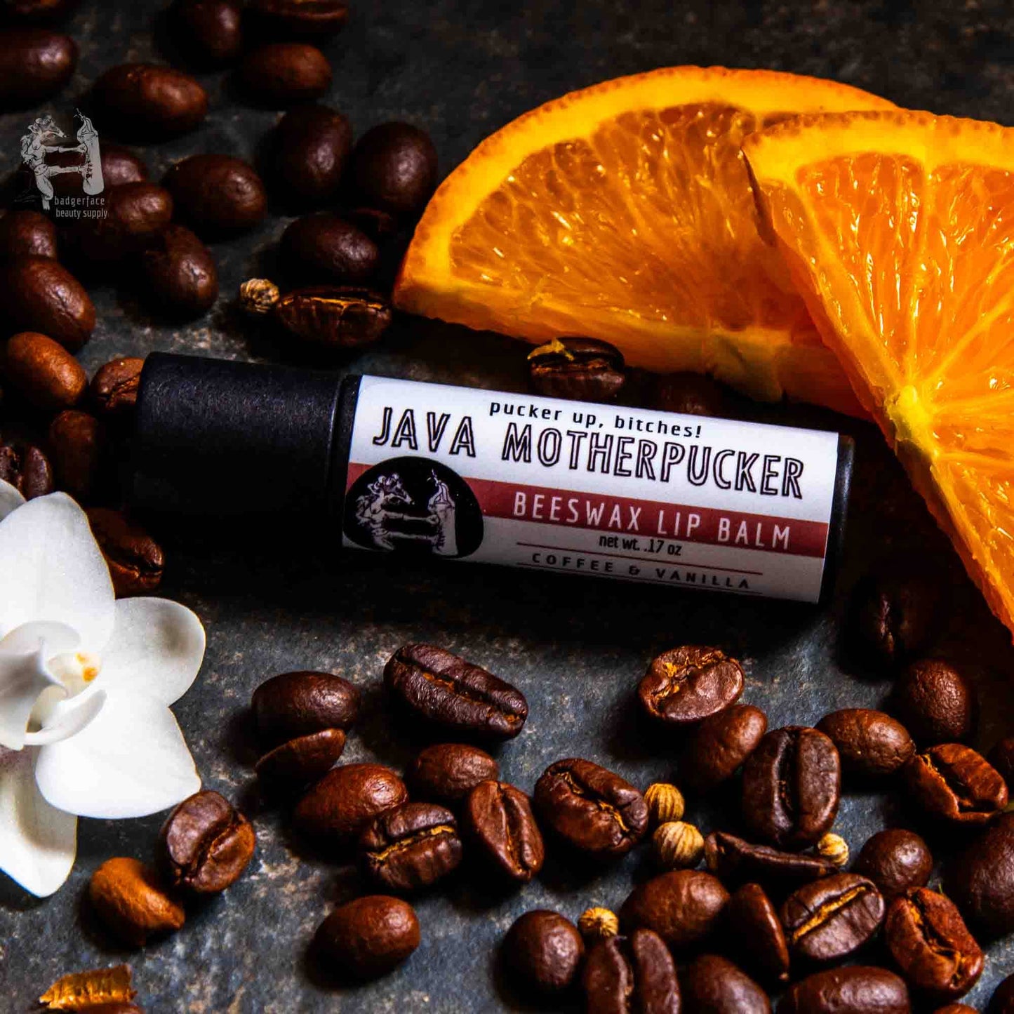 An earthy photo showing slices of orange, coffee beans and vanilla with a tube of Java Motherpucker lip balm. The label text shows, "Pucker up, bitches!"