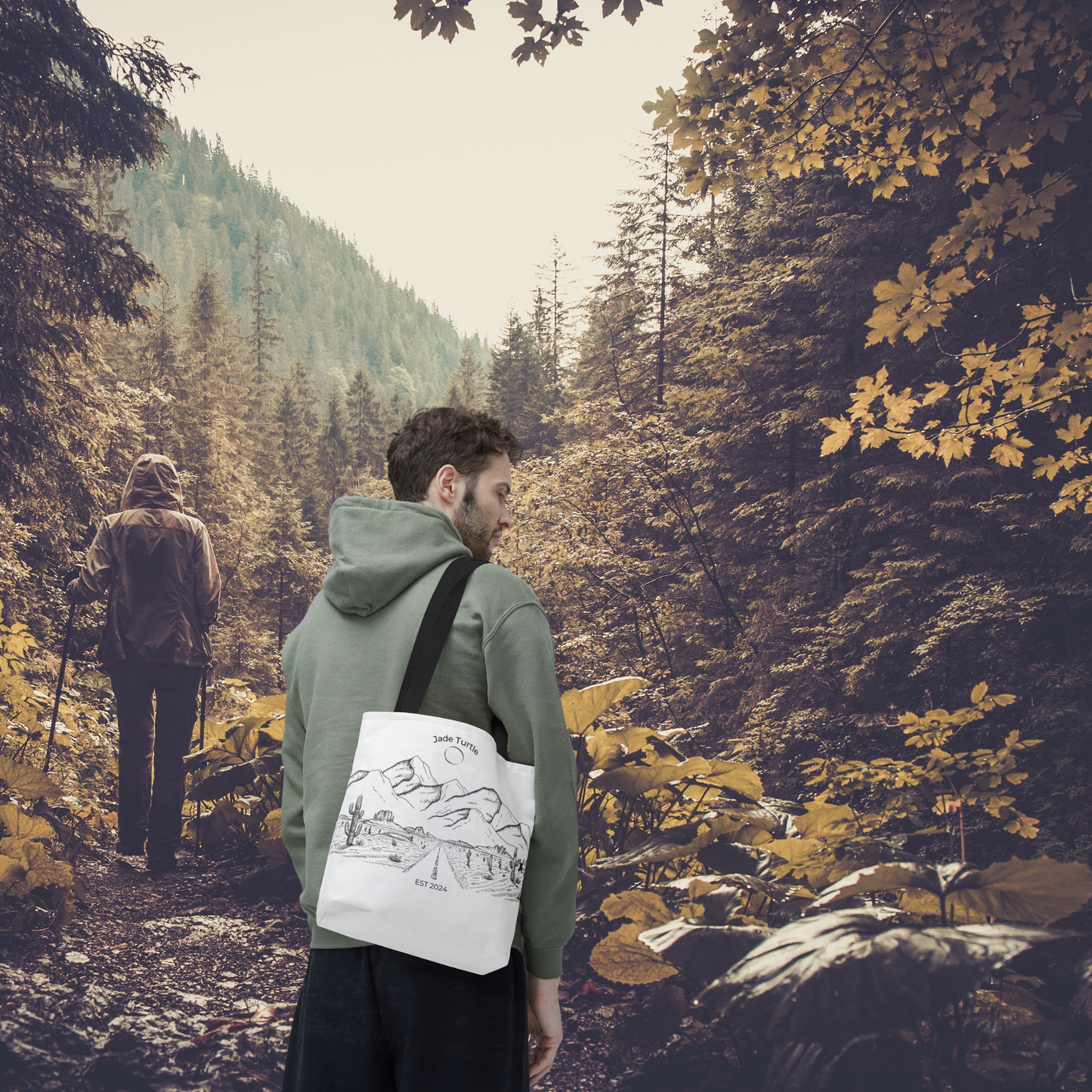 A young man in a hooded sweatshirt is carrying a Jade Turtle design Canvas Tote Bag with black handle while walking with a woman on a trail in the woods.