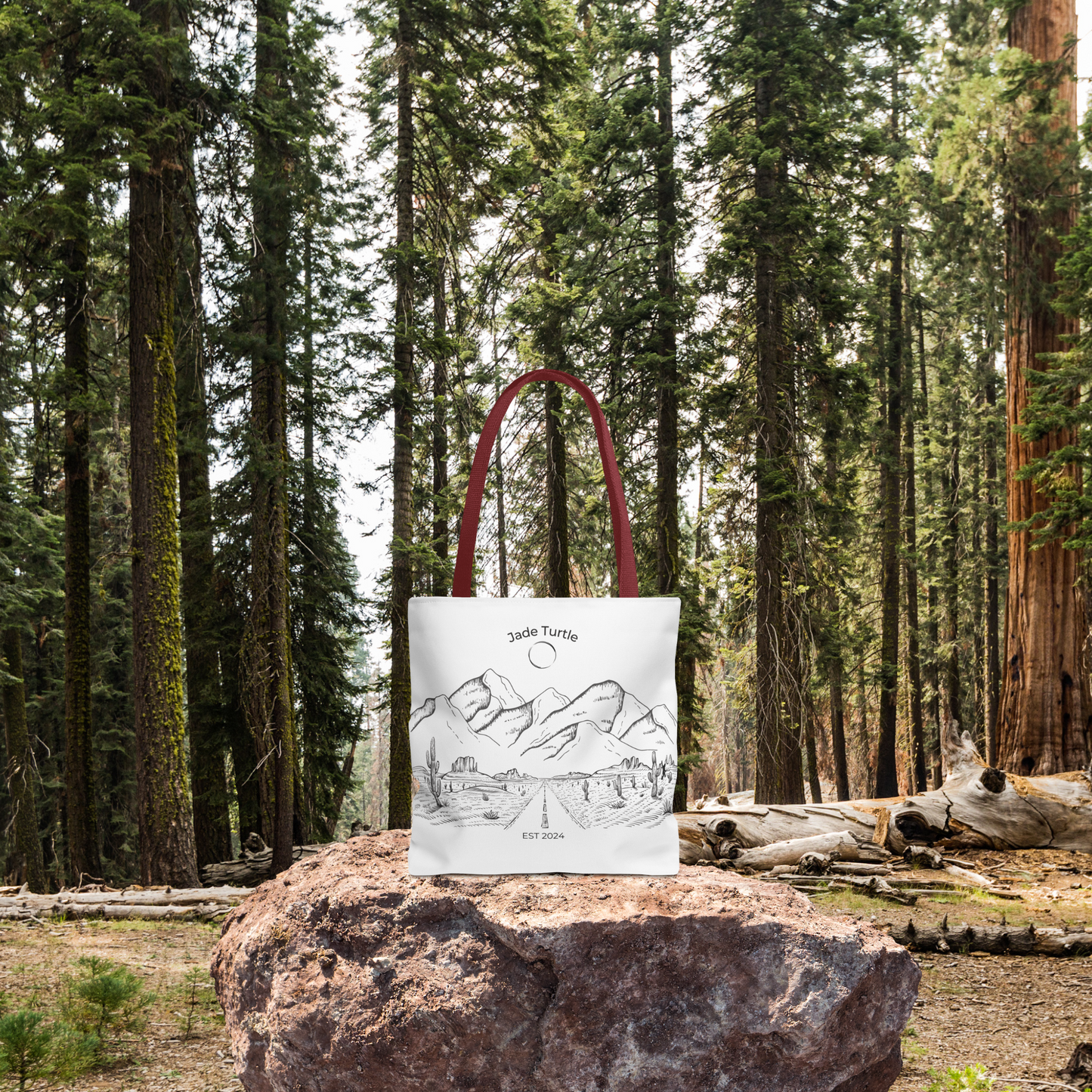 A Jade Turtle design canvas tote bag with red handle sits on a rock in a brightly lit wooded area.