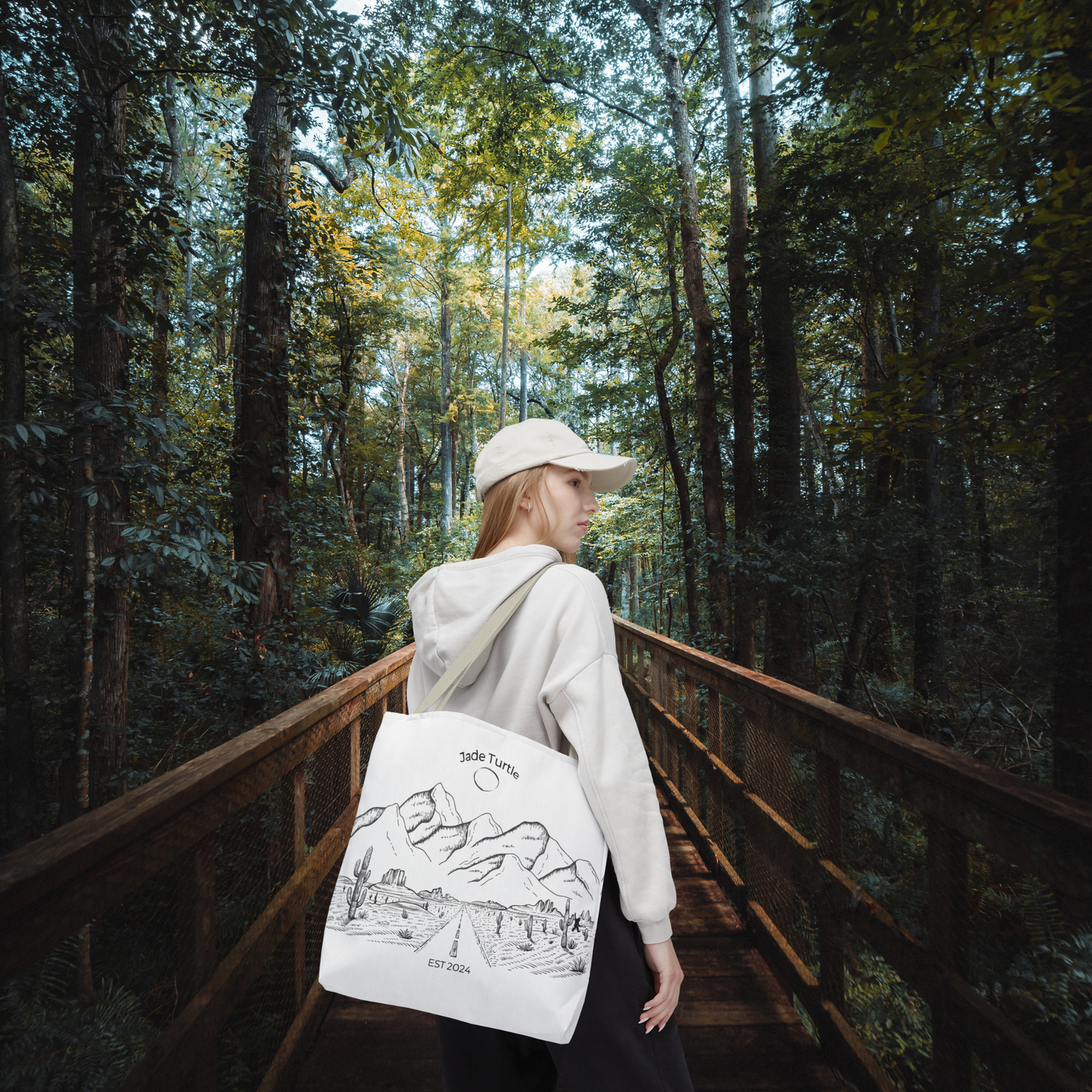 A young woman with ballcap and hooded sweatshirt is carrying a Jade Turtle design Canvas Tote Bag with beige handle while walking on a wooden bridge in the woods.