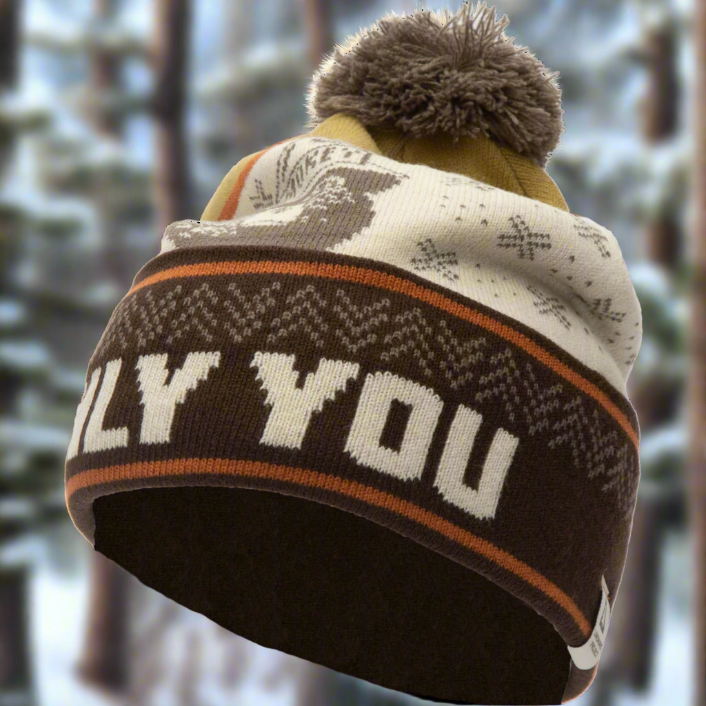 Smokey the Bear Only You pom beanie in brown, gold and cream is outside with blurred snowy winter trees in the background.