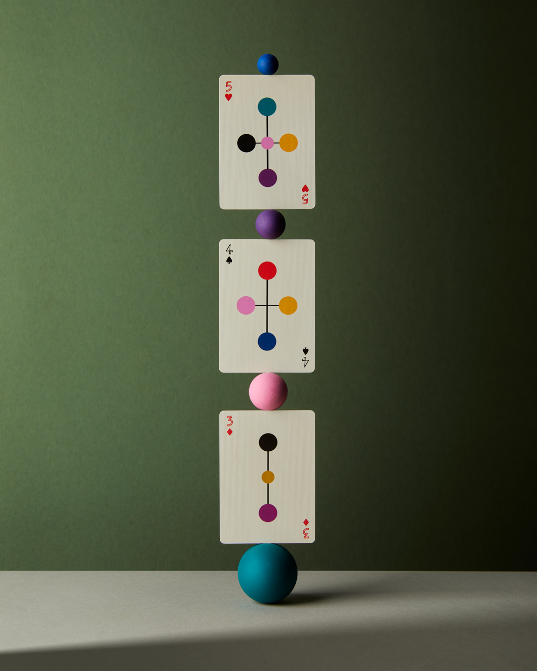 Three unique playing cards balanced end on end with small round colorful balls in between each card.