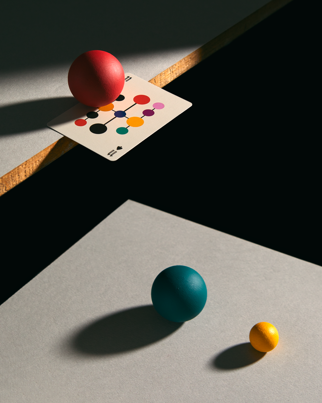 Colorful and artistic playing card on a wooden table with a red ball, a blue ball and a yellow ball.