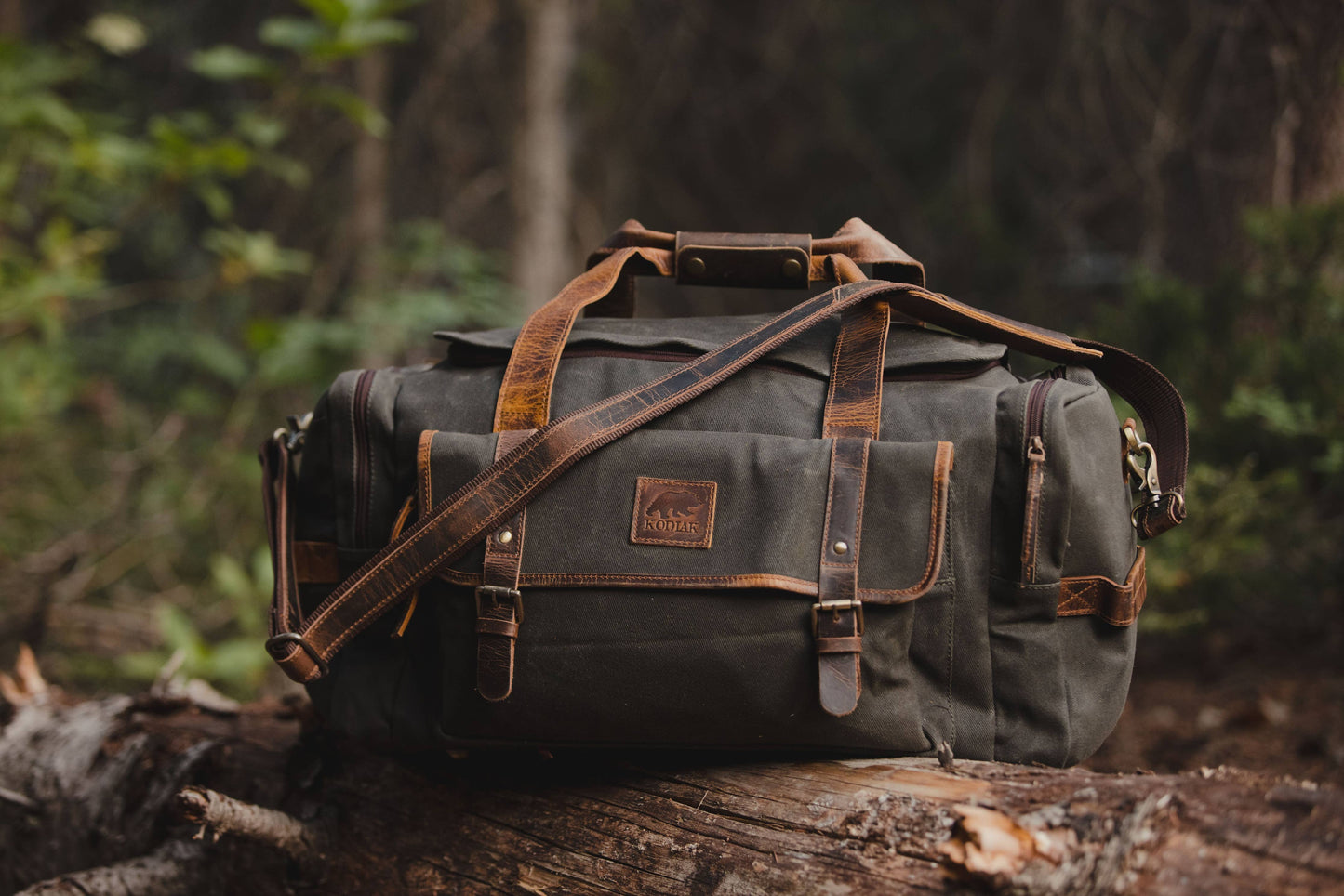 canvas and leather duffel sitting on a log in a woodsy environment