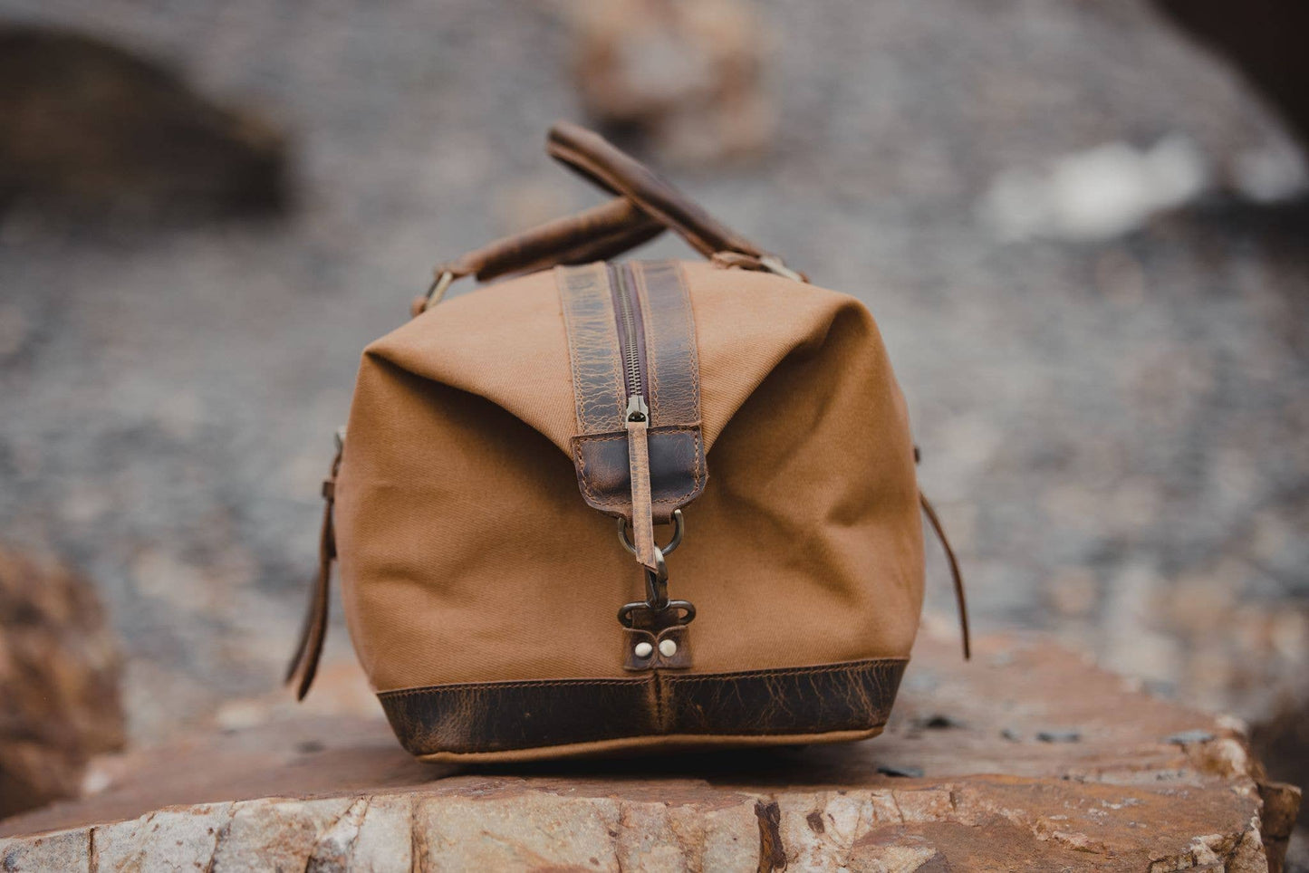 An end view of a tan canvas and leather duffel bag showing the leather trim and brass closures.