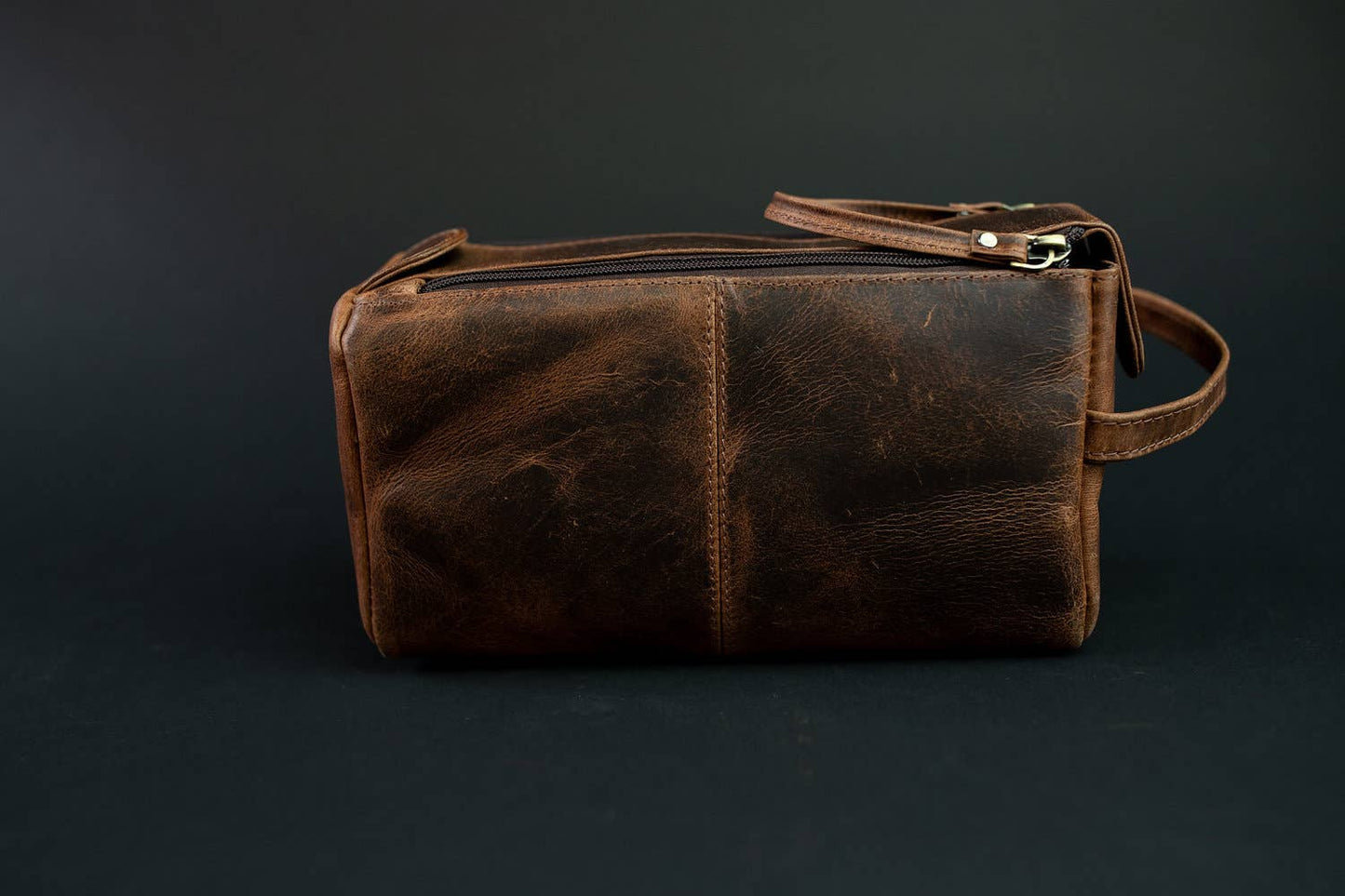 Back view of leather toiletry bag against a dark background.