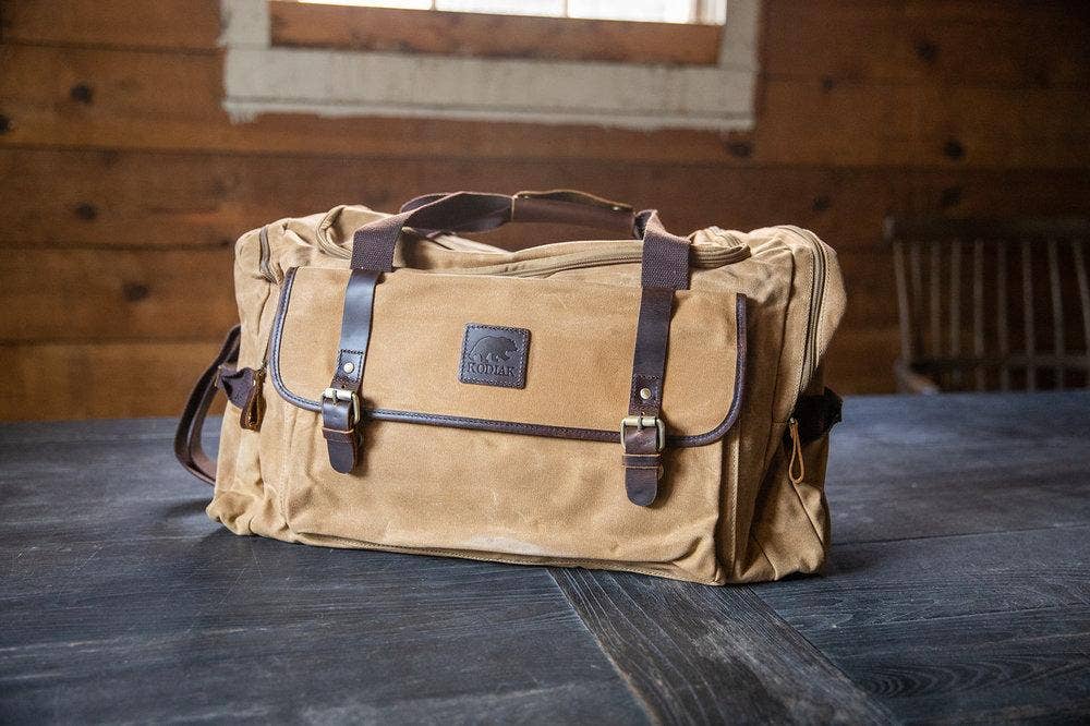 Photo of a tan canvas and leather duffel bag sitting on a wooden table inside a cabin.