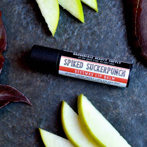 An earthy photo showing slices of green apple with a tube of Spiked Suckerpunch lip balm. The label text shows, "Pucker up, bitches!"