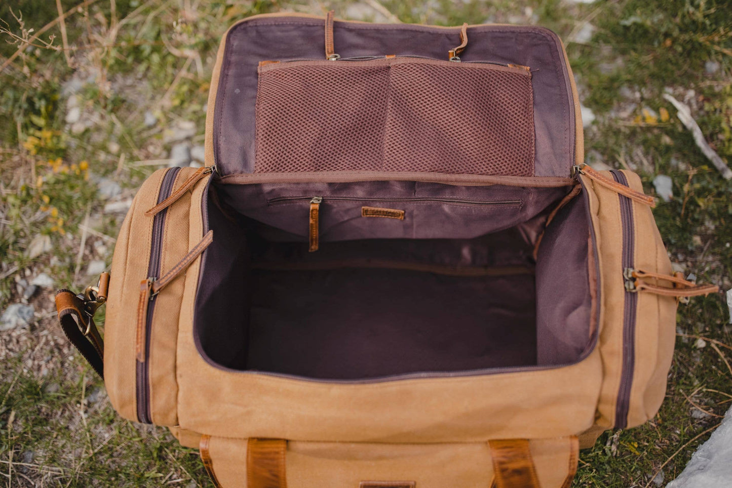 Open canvas and leather duffel bag showing interior compartment with zippered pockets inside.