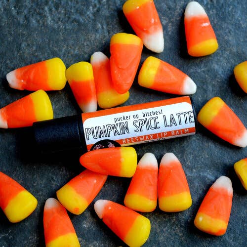 An earthy photo showing pieces of candy corn with a tube of Pumpkin Spice Latte lip balm. The label text shows, "Pucker up, bitches!"