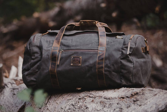 Green duffel bag with brown leather straps on a log in a forest setting