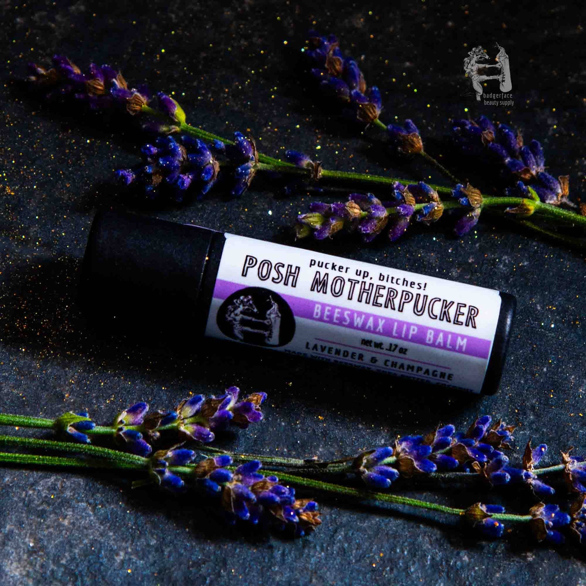 An earthy photo showing sprigs of lavender with a tube of Posh Motherpucker lip balm. The label text shows, "Pucker up, bitches!"